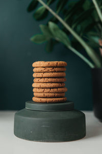 Stack of ginger biscuits displayed on a green pedestal with a dark green background and plant decor.